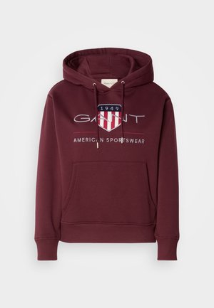 Maronfarvet hættetrøje lavet af blødt stof, med en frontlomme, snoretræk og et logo med et skjold og "1949" tekst på brystet.