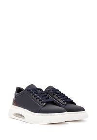 Sneakers in pelle blu navy con suola in gomma bianca, lacci rotondi e un accento marrone sul tallone; texture liscia e design a taglio basso.