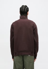 Sweat-shirt à col montant de couleur bordeaux, à la texture douce et à la coupe décontractée, associé à un pantalon cargo vert olive.