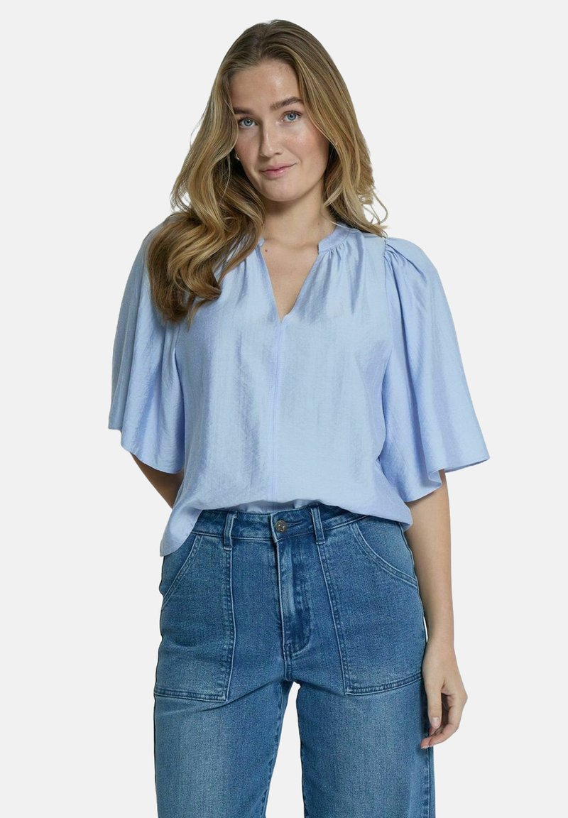 Haut bleu clair à manches courtes et décolleté en V avec un col plissé, fabriqué à partir d'un tissu doux, associé à un jean en denim bleu clair taille haute.