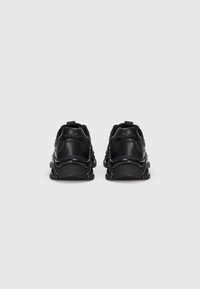 Baskets de sport noires avec des tiges synthétiques lisses, des accents texturés et des semelles en caoutchouc. Présentent des tirettes à l'arrière et une silhouette en chunky, arrondie.