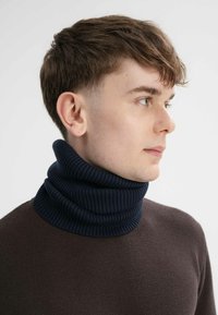 Donkerbruine trui met een dikke marineblauwe ribgebreide col. De col is omgeslagen, wat de textuur en het patroon van de stof benadrukt.