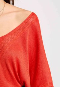 Felrood, ruime gebreide top met een brede halslijn en een gestructureerde stof. Heeft een off-shoulder ontwerp en flowy mouwen.