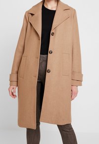 Manteau en mélange de laine camel avec un col cranté, un design croisé à double boutonnage et trois boutons. Comprend des poches latérales et une coupe décontractée.