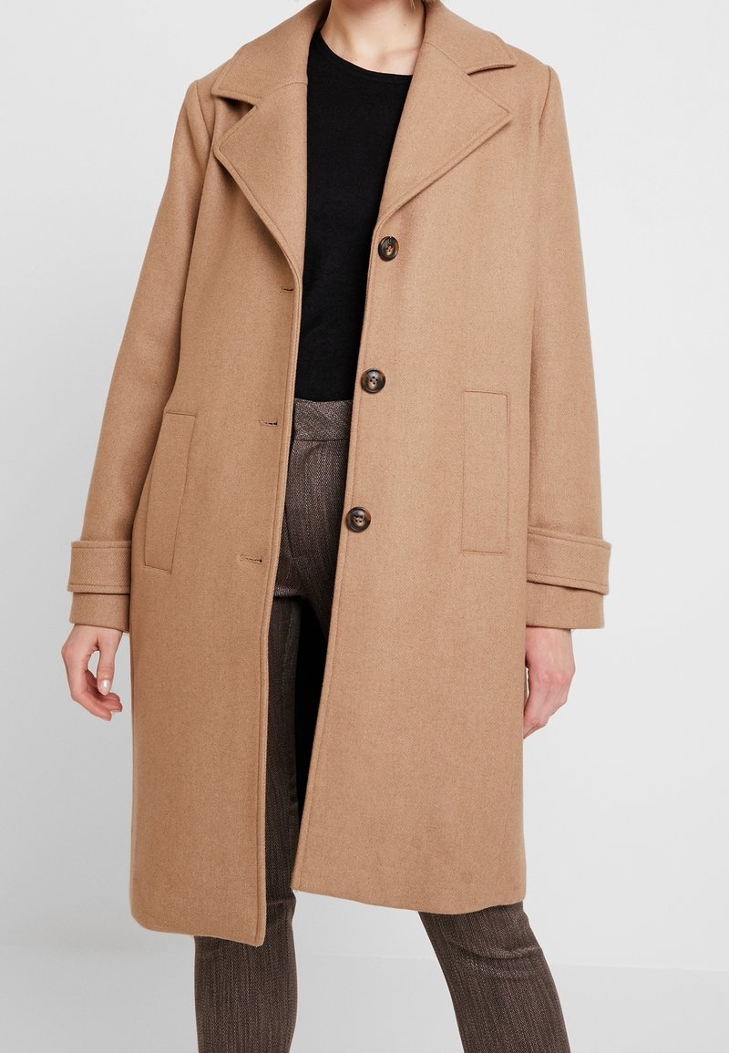 Manteau en mélange de laine camel avec un col cranté, un design croisé à double boutonnage et trois boutons. Comprend des poches latérales et une coupe décontractée.