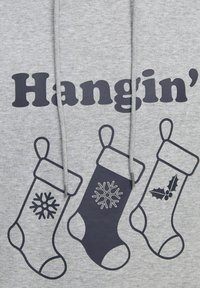 Sivi dukserica s natpisom "Hangin'" u podebljanim crnim slovima, koja sadrži tri crna božićna čarapa s uzorcima pahulja i božikovine.