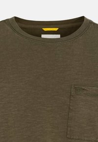 T-shirt marron col rond avec une petite poche cousue sur la poitrine gauche comportant un détail subtil de logo incurvé.