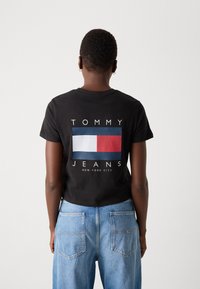 Svart bomullströja med korta ärmar som har en stor röd, vit och blå logotyp med texten "TOMMY JEANS NEW YORK CITY" på baksidan.