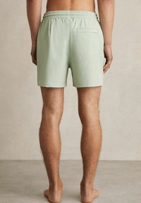 Shorts de bain pour hommes en vert clair, fabriqués en tissu léger. Équipés d'une taille élastique, d'une poche arrière et d'un design simple.