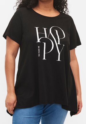 Frau trägt ein schwarzes T-Shirt mit großem weißem Schriftzug "HAPPY" und kleinem vertikalem Text "YOU MAKE ME", kombiniert mit blauer Jeans.