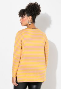 Maglietta a maniche lunghe con strisce orizzontali gialle e rosa, in tessuto morbido, colletto tondo e spacchi ai lati dell'orlo per facilitare il movimento.