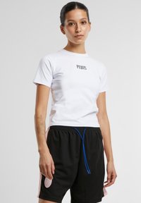 Camiseta blanca de manga corta con texto negro "PEQUS". Se lleva con pantalones cortos negros con detalles en rosa y un cordón azul. Textura suave.