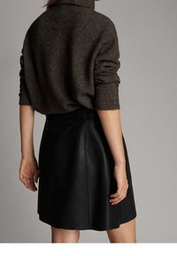 Mørkebrunt uldtrøje med høj krave og løse ærmer, parret med en tætsiddende sort lædernederdel, der viser en glat tekstur.