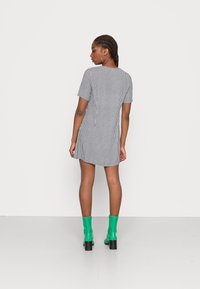 Vestido de mangas curtas em padrão xadrez preto e branco com um corte descontraído, combinado com botas verdes até ao joelho, visto de costas contra um fundo branco.