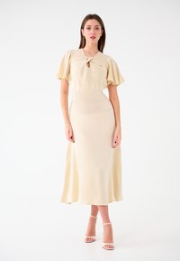Beige, midi-langes Kleid mit einem Schlüsselloch-Ausschnitt und kurzen, ausgestellten Ärmeln. Glatte Textur mit taillierter Passform. Getragen mit Riemchen-Hochzeiten.