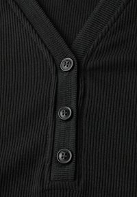 Svart ribbad tyg med tre svarta knappar, V-ringad söm och knapphål, närbild av texturerad stickad detaljer.