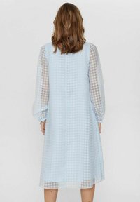 Svetlo modra obleka z teksturirano tkanino, houndstooth vzorcem in prozornimi dolgimi rokavi. Srednje dolga zasnova, oprijet bodice, sproščen kroj.