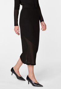 Jupe midi noire en tricot avec une texture côtelée et un design à fente, associée à des escarpins noirs à bout pointu. Coupe ajustée à la taille.