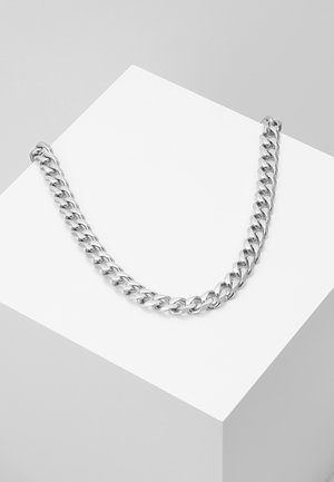 Collier épais à chaîne en argent avec des maillons entrelacés, présenté sur un socle géométrique blanc contre un fond gris.