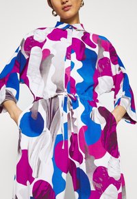 Chemise colorée avec des motifs abstraits en rose, bleu et blanc, dotée d'un col, de manches longues et d'une taille à cordon de serrage pour un ajustement parfait.