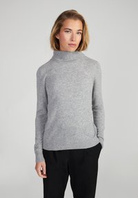 Maglione a collo alto grigio chiaro realizzato in morbida lana, con maniche lunghe e design aderente. Polsini e orlo a coste aggiungono texture.