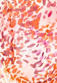 Satiinikangas, jossa on vesivärimaalauksen kaltainen abstrakti kuvio vaaleanpunaisen, oranssin ja punaisen sävyissä, nesteenomaisilla siveltimen vedoilla.