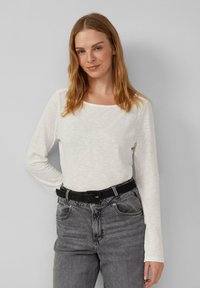 Haut à manches longues, couleur ivoire, en tissu doux et texturé, avec un col carré, associé à un pantalon en denim gris taille haute et une ceinture noire.