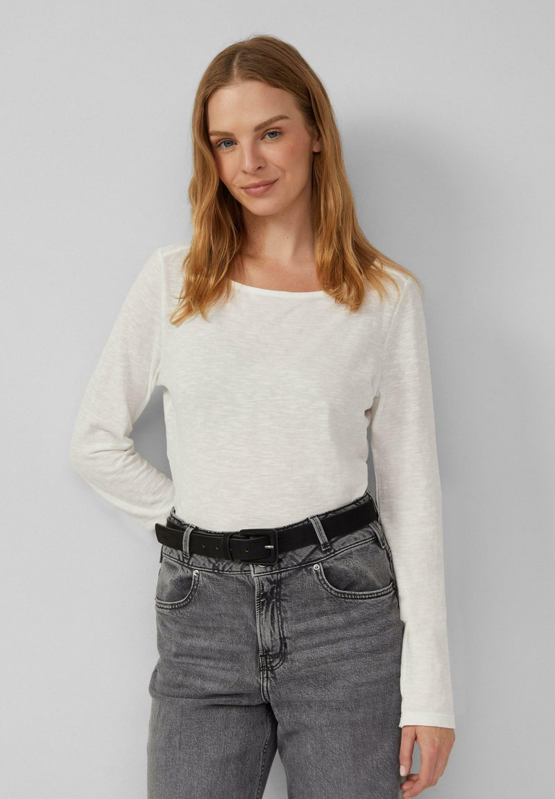 Haut à manches longues, couleur ivoire, en tissu doux et texturé, avec un col carré, associé à un pantalon en denim gris taille haute et une ceinture noire.