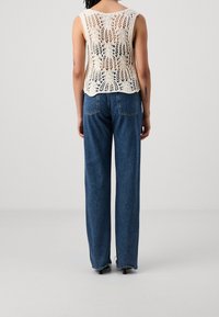 Top a maglia color crema con un design in pizzo, abbinato a jeans in denim blu a vita alta con orli sfilacciati e tasche posteriori.
