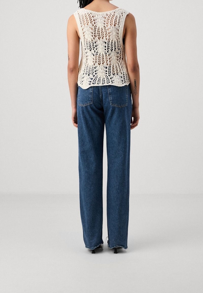 Top a maglia color crema con un design in pizzo, abbinato a jeans in denim blu a vita alta con orli sfilacciati e tasche posteriori.
