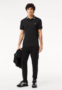 Zwarte polo met een gestreepte kraag, logo op de borst, gecombineerd met zwarte sweatpants en sneakers. Textuurstof, atletische pasvorm.