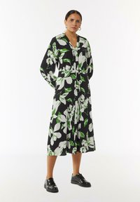 Schwarzes, blumiges Midikleid mit großen weißen und grünen Blumenmustern; ausgestattet mit einer Knopfleiste, V-Ausschnitt und langen Puffärmeln.