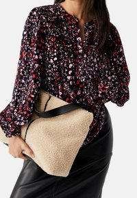 Blusa nera con bottoni caratterizzata da una stampa astratta colorata nei toni del rosa e del rosso; abbinata a una morbida borsa beige testurizzata con una tracolla nera.