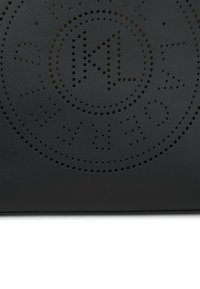 Sac en cuir noir avec un design circulaire perforé incluant des éléments textuels et une texture lisse. Détail de logo notable au centre.