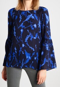 Námořnická blůza s modrým květinovým vzorem, zvonovými rukávy a kulatým výstřihem, vyrobená z lehkého materiálu. Viditelné švy na ramenou.