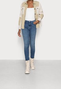 Chaqueta camisa bicolor en beige y blanco con grandes bolsillos de solapa, combinada con jeans ajustados azules y botas de combate crema con cordones.