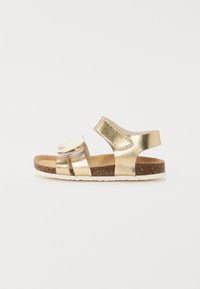 Guldmetalliska sandaler med korksula, utrustade med två remmar och en dekorativ blomaccent på framsidan. Justerbar kardborrestängning.