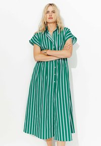 Robe chemise verte à rayures avec des manches courtes, un bouton sur le devant et une coupe décontractée. Présente des rayures verticales blanches et une longueur jusqu'aux genoux.