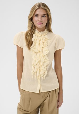 Gul bluse med flæsedetalje foran, korte pufærmer og høj halsudskæring. Letvægtsstof og knaplukning foran.