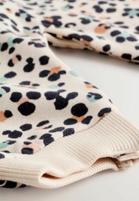 Sweatshirt à motif léopard avec un fond crème et des taches noires, pêche et menthe. Tissu doux avec des poignets côtelés.