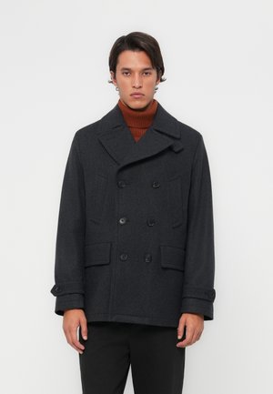 Manteau de marin en laine gris foncé avec un design croisé, de grands boutons et deux poches latérales. Présente de larges revers et un col roulé côtelé en dessous.