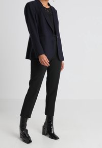 Marinfärgad blazer med en enkel knapp, slagkrage och skräddarsydd passform, i kombination med svarta byxor och blanka klackboots.