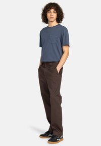 Navy blue short-sleeve t-shirt with a chest pocket, paired with brown trousers and black sneakers featuring white accents and gum soles.