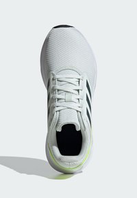 Baskets de sport blanches avec un dessus en mesh respirant, des accents noirs, trois bandes noires et un détail de semelle verte prononcé.