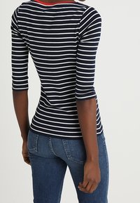 Navy and white striped shirt with three-quarter sleeves and red neckline detail, paired with blue jeans, showing back view and smooth texture.