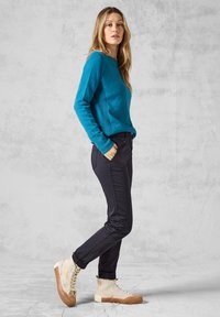Pull turquoise avec des détails côtelés, associé à un pantalon slim noir et des baskets montantes beiges avec des accents texturés et des semelles en caoutchouc.