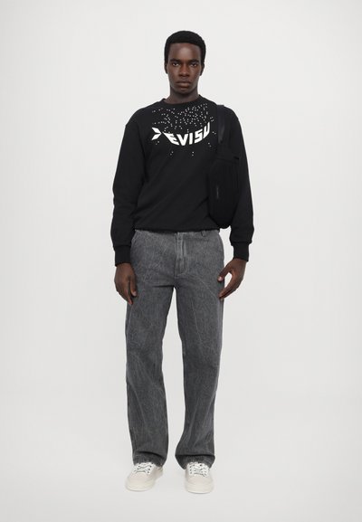 Sweatshirt noir avec le logo "Evisu" et un design texturé, pantalon en denim gris avec un aspect décoloré, et baskets blanches. Sac noir réglable porté en bandoulière.