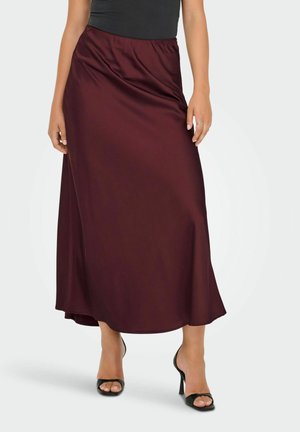 Femme portant une jupe midi en satin bordeaux foncé avec un haut noir sans manches et des sandales à talons ouverts noires.