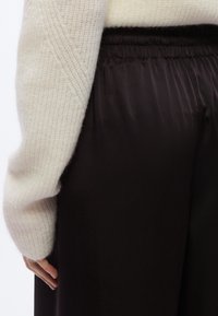 Pull en maille crème à coupe ample, associé à un pantalon large en satin noir avec une taille élastique.