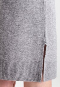 Robe grise en maille avec ourlet côtelé, dotée de fentes latérales et d'une texture douce. La structure met en valeur les coutures et le design global décontracté.